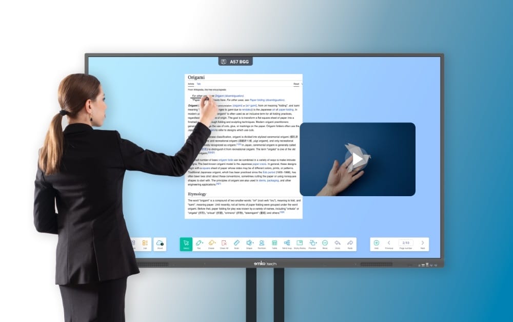 Siyah takım elbiseli bir kadın, metin ve kağıt tutan bir el görüntüsü gösteren, dijital bir beyaz tahtaya veya sunuma benzeyen büyük bir interaktif dokunmatik ekranda yazıyor.